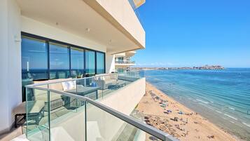 A modern hotel balcony with glass railings overlooking a beach and the sea.