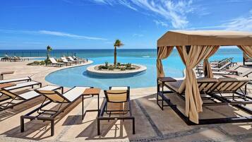 Un espace aménagé au bord de la piscine, avec des chaises longues et un coin salon couvert offrant une vue sur l’océan.