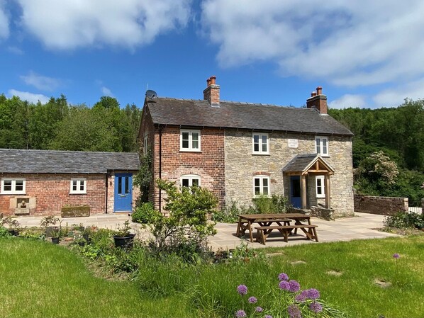 A stone cottage with a blue door, a small garden, and a picnic table.