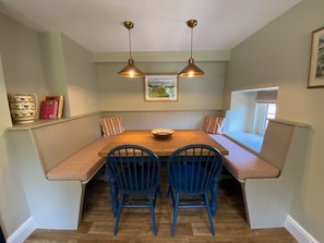 Un coin repas avec une table en bois, deux chaises bleues et un banc doté de coussins à rayures.