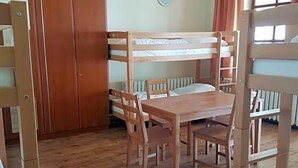A bunk bed room with a wooden table and chairs, a wardrobe, and a window with curtains. - Wichernhaus-Boltenhagen (Boltenhagen)