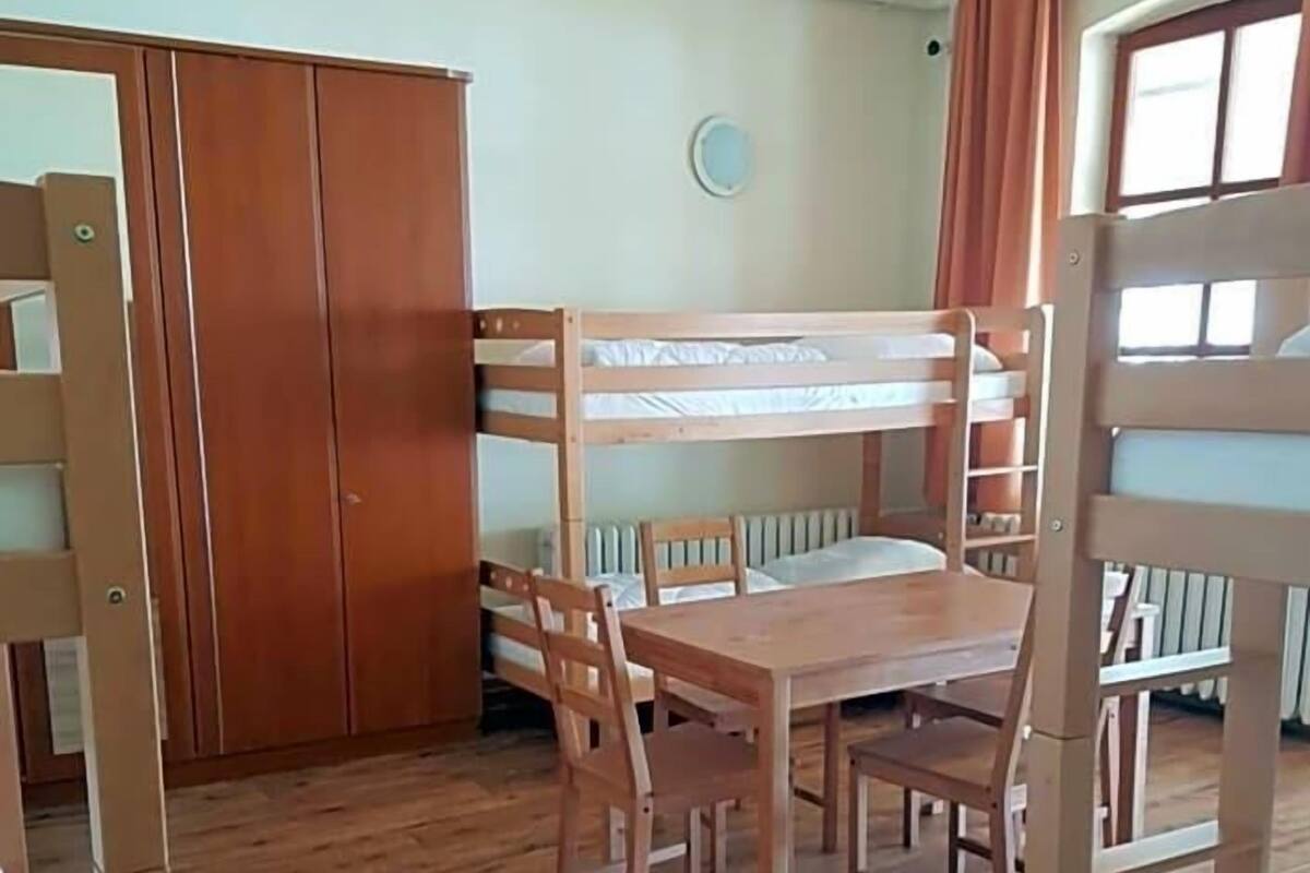 Ein Schlafraum mit Etagenbetten, einem Holztisch und Stühlen, einem Kleiderschrank und einem Fenster mit Vorhängen.