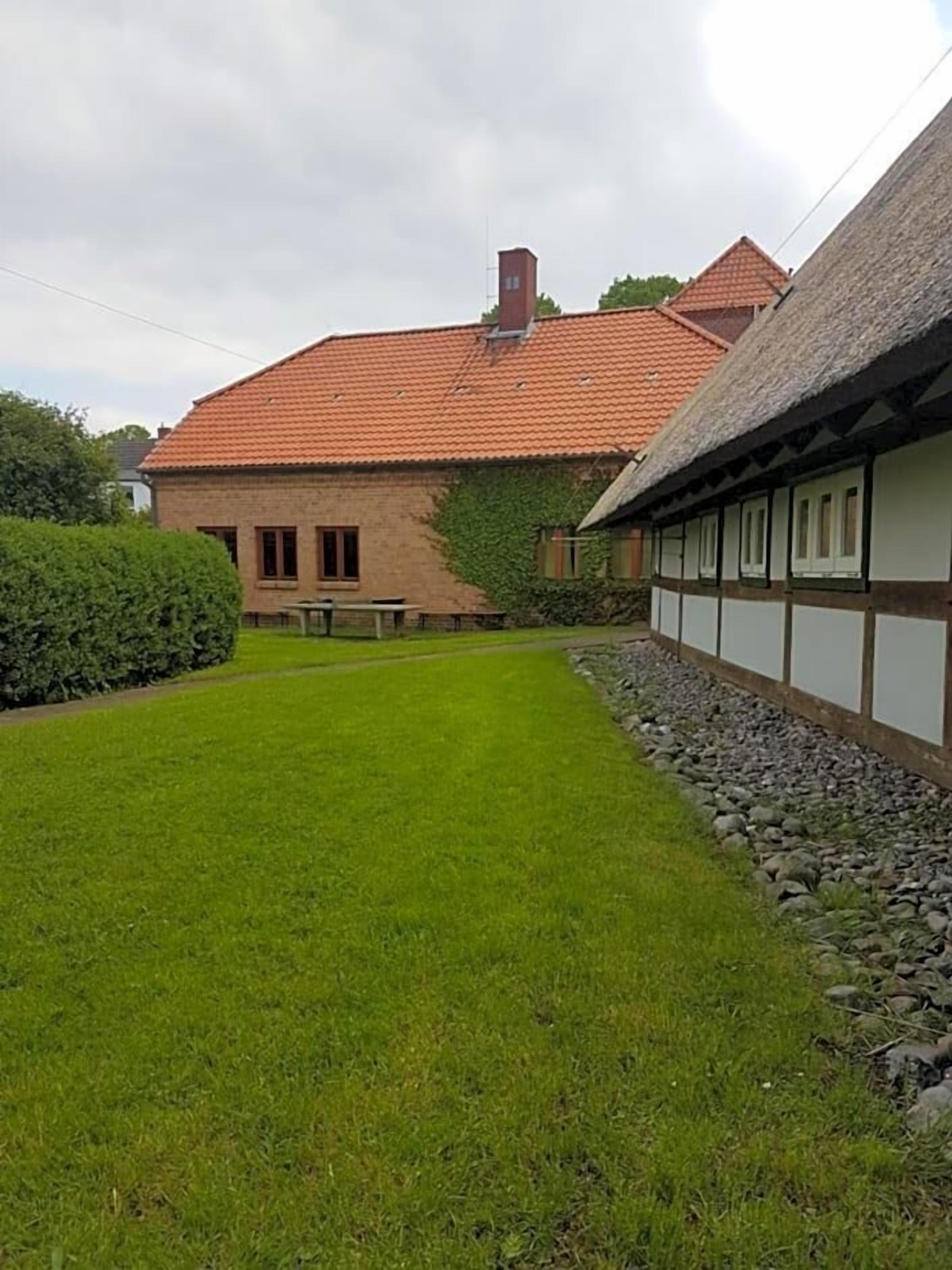 Ein traditionelles Haus mit rotem Ziegeldach, einem Anbau mit Strohdach und einem gepflegten Rasen.