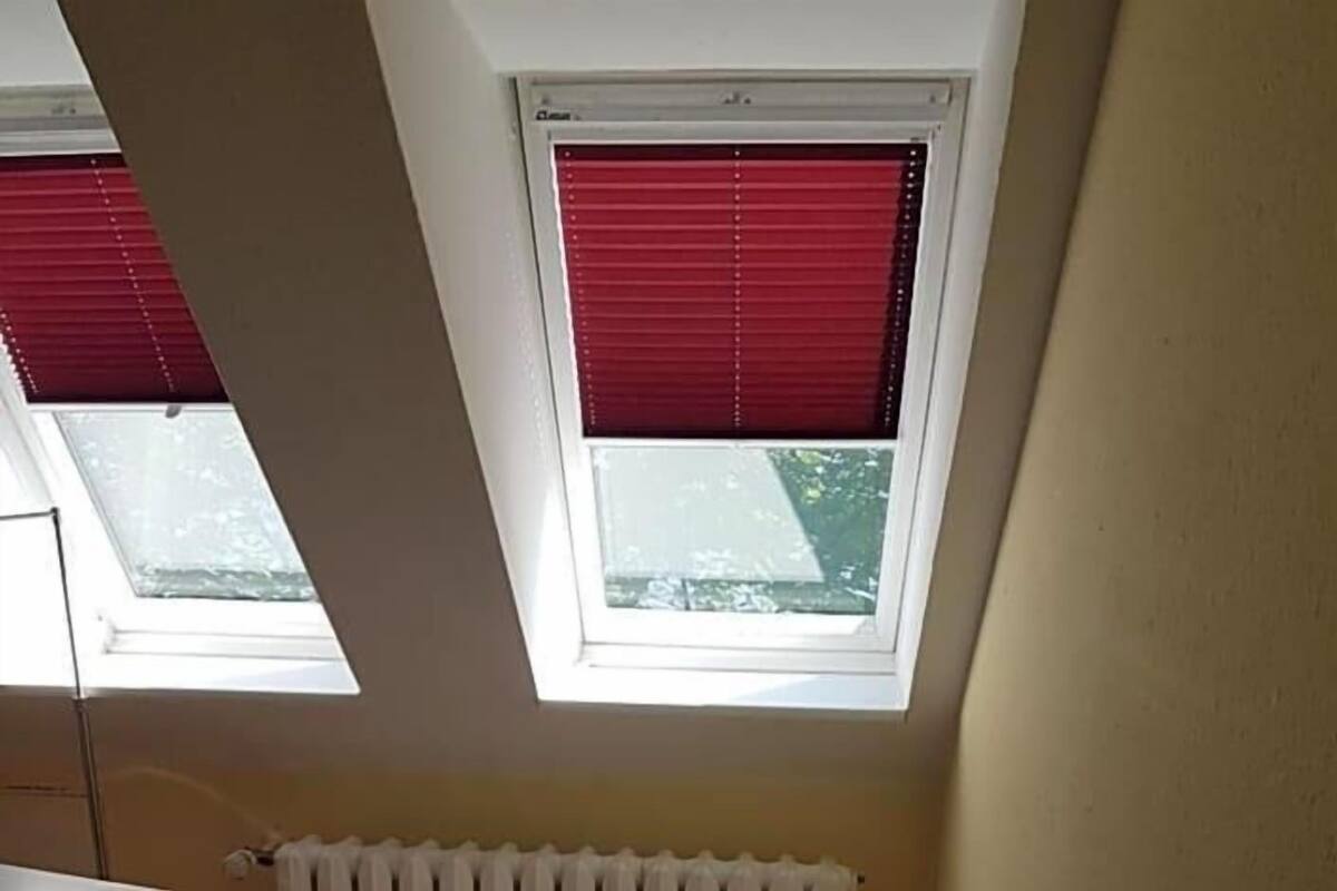 Ein kleines Zimmer mit einem Einzelbett, schrägen Wänden und Dachfenstern.