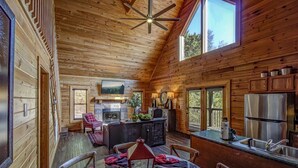 A wooden cabin interior with a dining area, kitchen, and a fireplace. - *Cozy 2BR + LOFT! • Game Room • HOT TUB! • Arcade* (Sevierville)