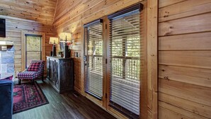 A wooden cabin interior with a fireplace, checkered chair, and large windows with blinds. - *Cozy 2BR + LOFT! • Game Room • HOT TUB! • Arcade* (Sevierville)