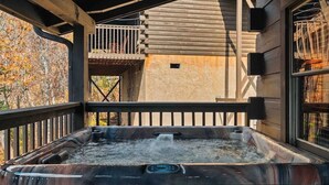 A hot tub with a wooden deck, a wooden cabin in the background, and a view of trees. - *Cozy 2BR + LOFT! • Game Room • HOT TUB! • Arcade* (Sevierville)