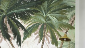 Una habitación con piso de madera, una mesa redonda, dos sillas amarillas y un mural en la pared con palmeras.