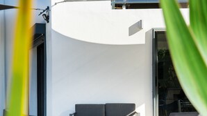 An outdoor seating area with modern furniture, a glass table, and a view of the building's interior. - L'Escapade Bellepierre (Saint-Denis)