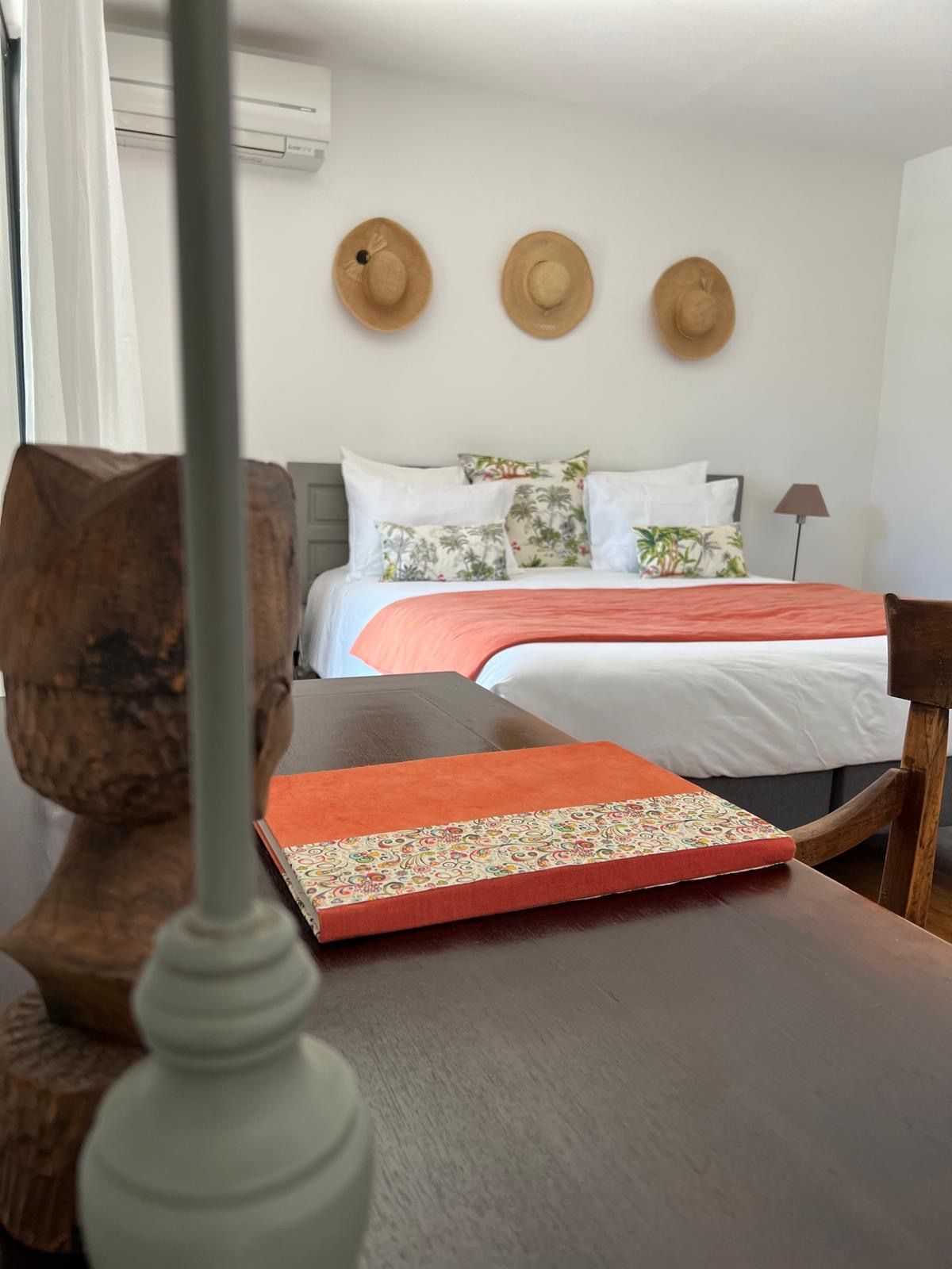 Une chambre d’hôtel avec un lit, des oreillers, une table de chevet, une lampe et un chapeau accroché au mur.