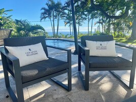 Dos sillones de exterior con cojines, una piscina y vistas al océano.