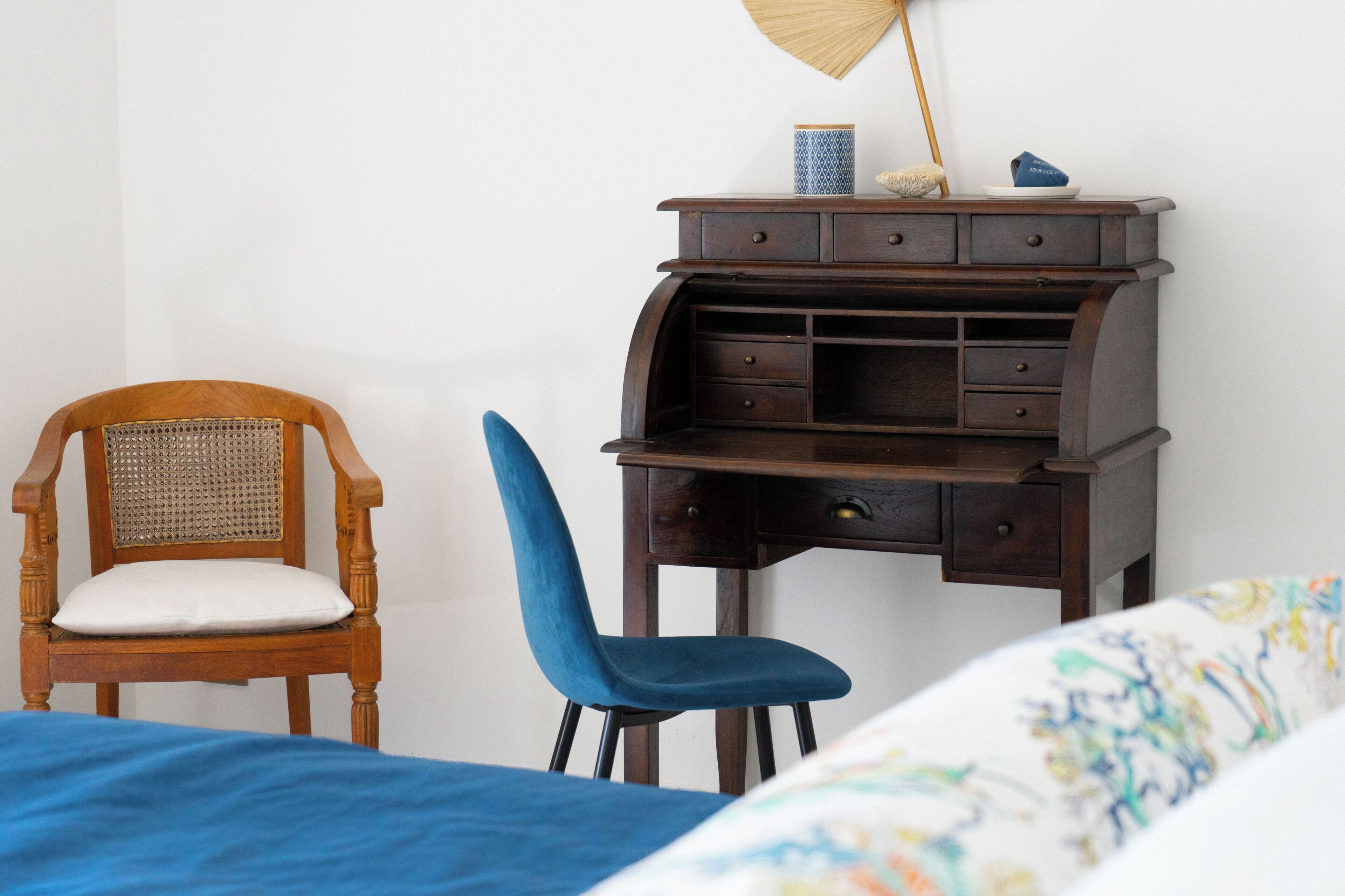 Un dormitorio con una cama, una silla de madera, un escritorio con cajones y una lámpara fijada a la pared.