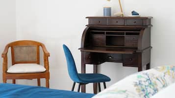 Un dormitorio con una cama, una silla de madera, un escritorio con cajones y una lámpara fijada a la pared.