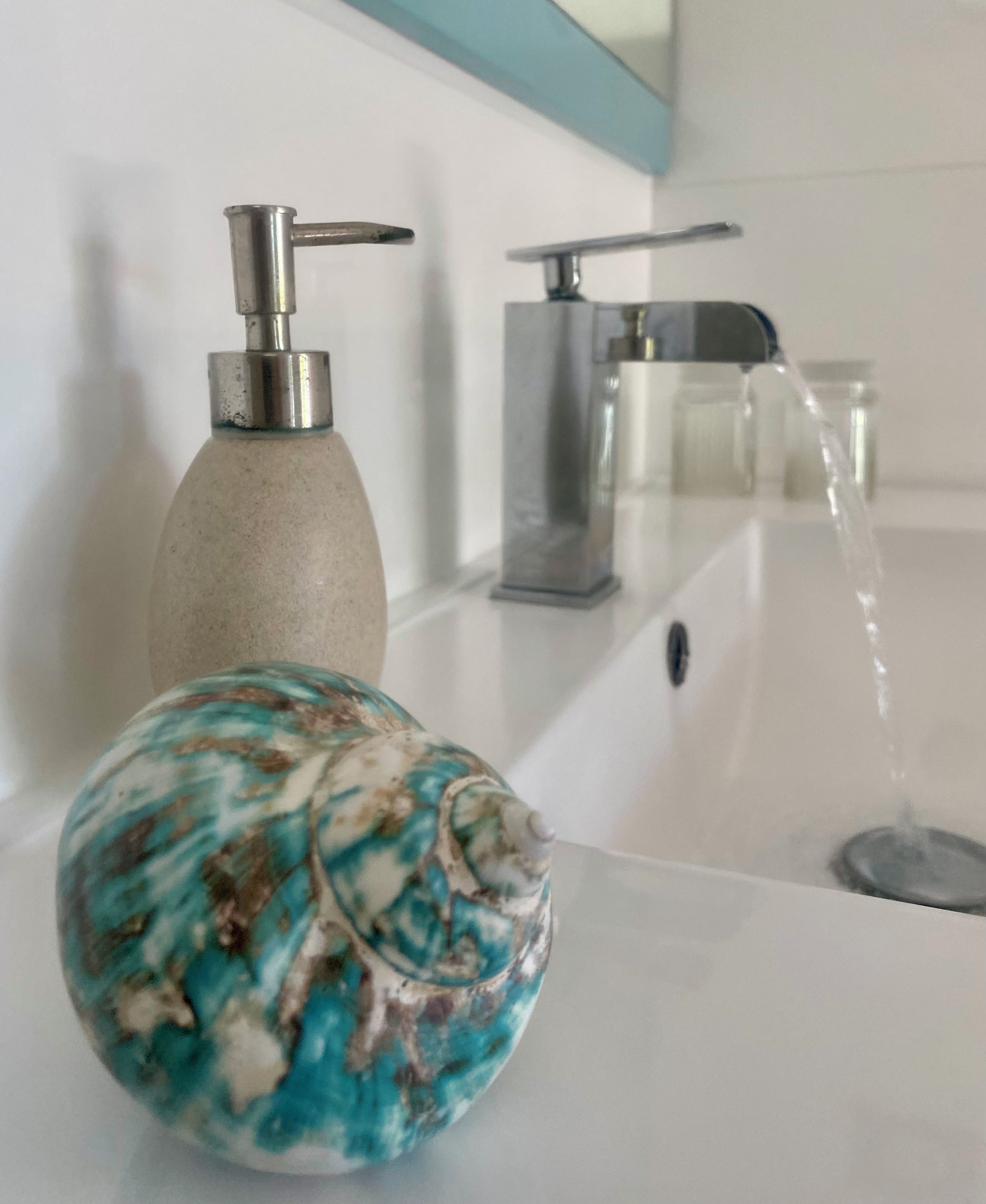 A bathroom with a white sink, a soap dispenser, and a decorative stone.