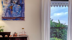 A room with a bed, a desk with a chair, a painting on the wall, and a window with curtains. - L'Escapade Bellepierre (Saint-Denis)