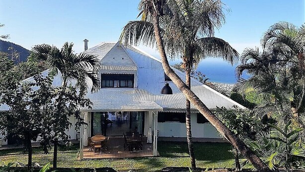 A house with a corrugated metal roof, a covered porch, and palm trees in the foreground. - L'Escapade Bellepierre (Saint-Denis)
