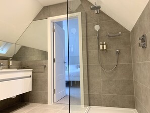 A modern bathroom with a shower, a glass door leading to a bedroom, and a large mirror. - Trewhiddle Villa 13 (St Austell)
