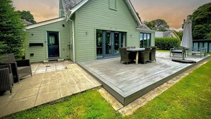 A green house with a patio, a dining area, and a covered outdoor seating area. - Trewhiddle Villa 13 (St Austell)