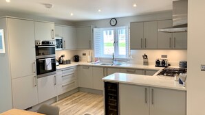 A modern kitchen with built-in appliances, a central island, and a window providing natural light. - Trewhiddle Villa 13 (St Austell)