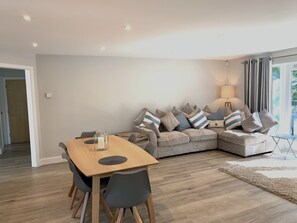 A modern living room with a wooden dining table, grey sofa with striped cushions, and a lamp. - Trewhiddle Villa 13 (St Austell)
