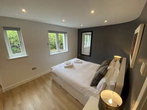 Ein Schlafzimmer mit einem Bett, zwei Fenstern, einem Nachttisch mit Lampe und einem Spiegel an der Wand.