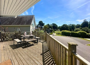 Eine Holzterrasse mit Gartenmöbeln, ein Gebäude mit Giebeldach und ein klarer Himmel.