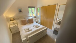 Een slaapkamer met een groot bed, nachtkastjes, een kledingkast en een spiegel.