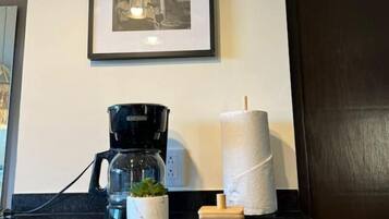 A framed black and white photograph on the wall, a coffee maker, a roll of toilet paper, and a small plant on a reflective surface.