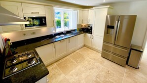 Een moderne keuken met witte kastjes, roestvrijstalen apparatuur, een gasfornuis en een raam dat voor natuurlijk licht zorgt.