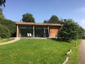 A modern building with large glass windows, a wooden exterior, and a grassy lawn with dandelions. - Yorkshire Dales Lodge 1 Ensuite 3 Bed (Richmond)