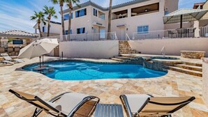 Un área de piscina con sillones de descanso, un jacuzzi y una escalera que conduce a un edificio con balcones.