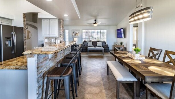 Una cocina moderna con encimeras de granito, una zona de comedor con una mesa de madera alargada y una barra con taburetes.