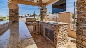 Una cocina exterior con encimera de piedra, una parrilla y un ventilador de techo.