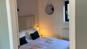 A bedroom with a bed, pillows, a bedside lamp, a window, and a wall-mounted circular mirror. - Yorkshire Dales Lodge 5 Family (Richmond)