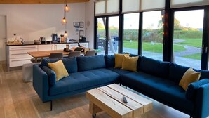 A modern living room with a large blue sectional sofa, a wooden coffee table, and a kitchen area with a dining table. - Yorkshire Dales Lodge 5 Family (Richmond)