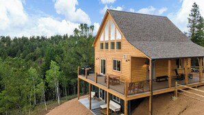 A two-story log cabin with a balcony, surrounded by a forest. - Alpine Escape: Family-Friendly Cabin with Spectacular Views (Divide)