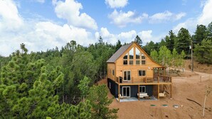 A two-story wooden cabin with a balcony, surrounded by dense pine trees. - Alpine Escape: Family-Friendly Cabin with Spectacular Views (Divide)