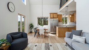 A modern kitchen with wooden cabinets, a stainless steel refrigerator, and a dining area with a table and chairs. - Alpine Escape: Family-Friendly Cabin with Spectacular Views (Divide)