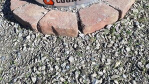 Un foyer extérieur en métal, orné d’un logo en forme d’étoile et de l’inscription « COUNTYLINE », entouré d’une base en briques et posé sur une surface de gravier.
