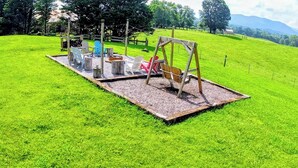 Une aire de jeux avec des balançoires, un toboggan et une petite table entourée de chaises.