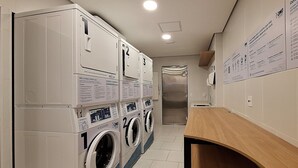 Een wasserette met meerdere wasmachines en drogers, een houten toonbank en instructieposters aan de muur.