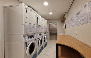 Una sala de lavandería con varias lavadoras y secadoras, una encimera de madera y carteles instructivos en la pared.