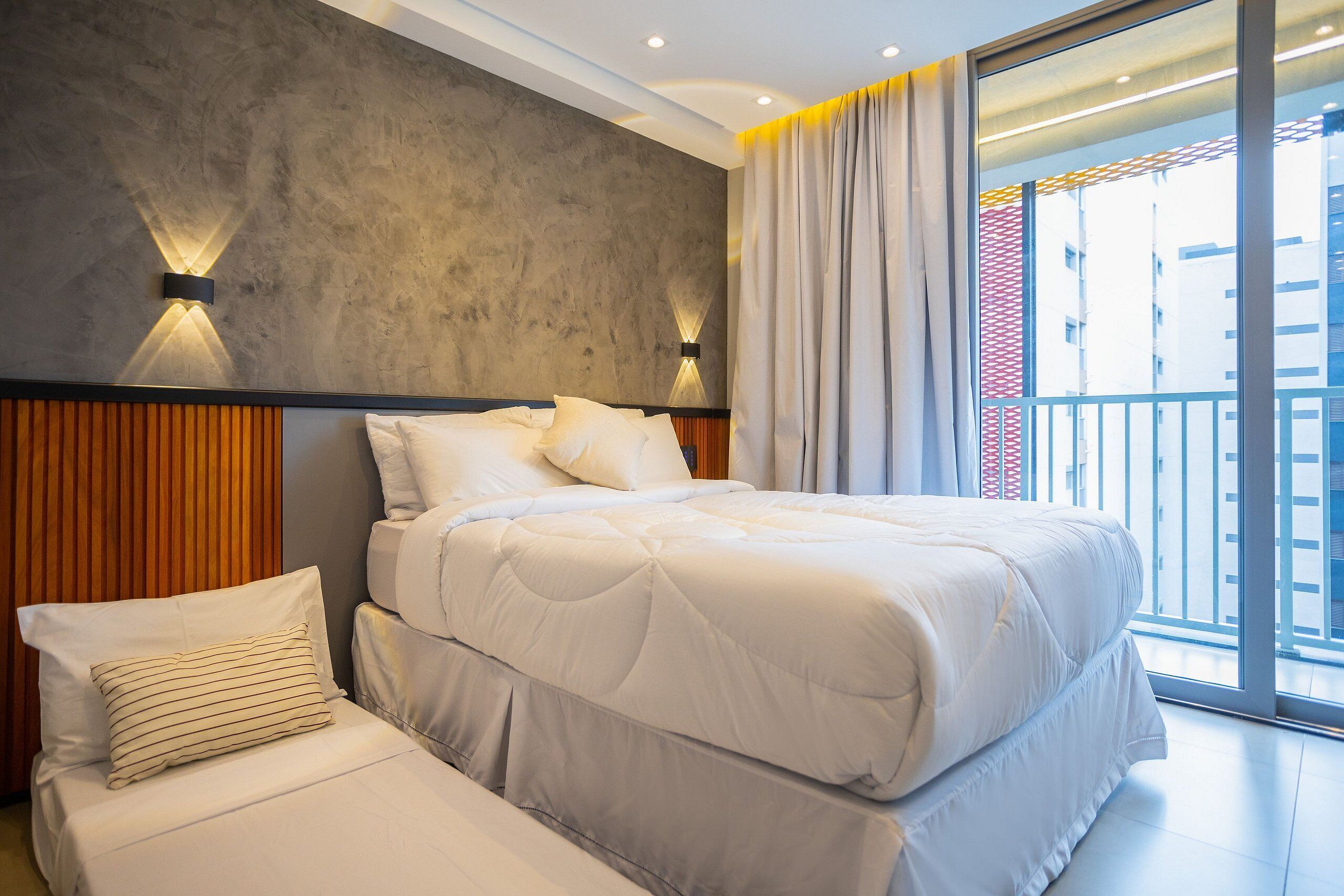 Habitación de hotel moderna con una cama grande, cabecera de madera y vista a la ciudad desde el balcón.