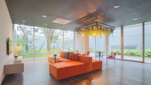 Een ruime woonkamer met een grote oranje bank, een hangende plantenlamp en uitzicht op de omgeving.