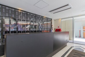 A reception desk with a modern design, a glass wall with a cityscape view, and a clear glass partition. - On Imarés (São Paulo)
