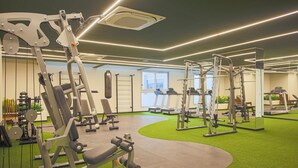Een fitnessruimte met diverse trainingsapparaten, een vloer van kunstgras en een groot raam voor natuurlijk licht.