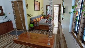 A hallway with a wooden swing, a dining area with a sofa and chairs, and a kitchen area with a sink and cabinets. - Oyster Marris Homestays in Trivandrum (Thiruvananthapuram)