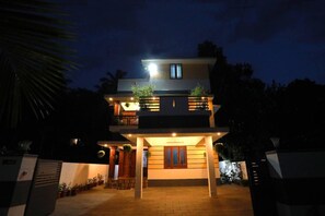 A two-story house with a balcony, potted plants, and a well-lit entrance. - Oyster Marris Homestays in Trivandrum (Thiruvananthapuram)