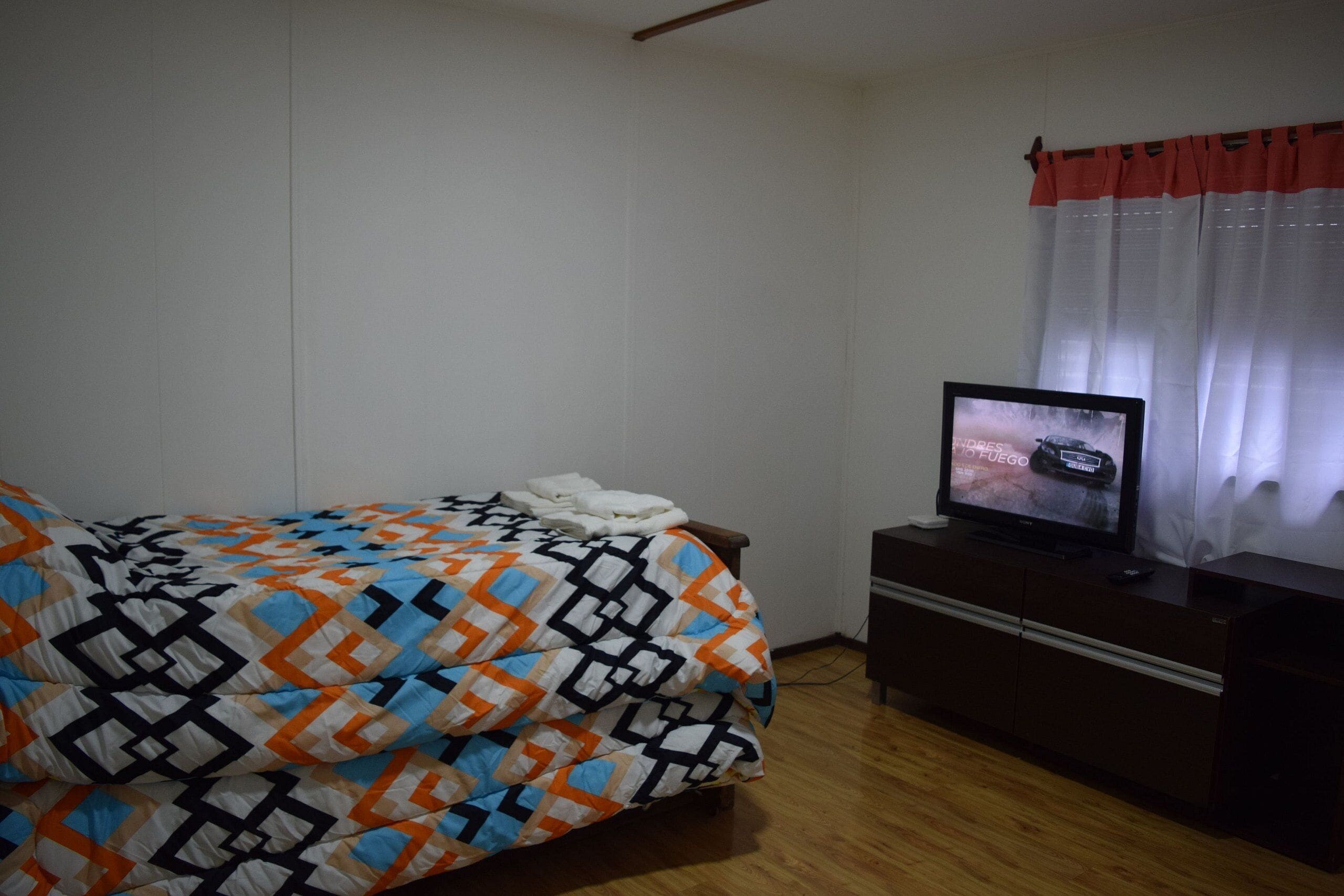 A bedroom with a bed, a TV on a dresser, and a window with curtains.