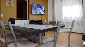 Ruokailutila, jossa on pöytä, tuolit ja seinälle asennettu televisio.